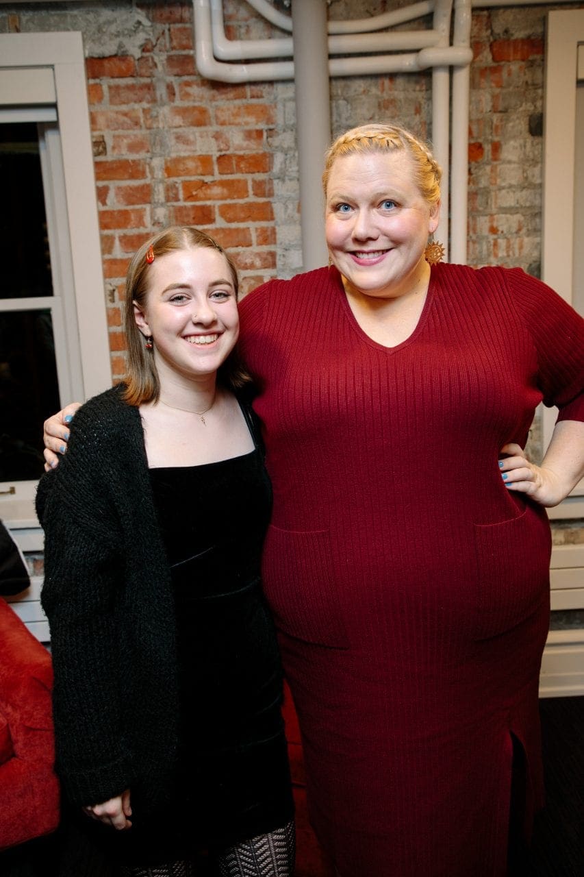 Lindy West stands with her arm over the shoulder of a smiling young student reader. They're standing in front of a brick wall.