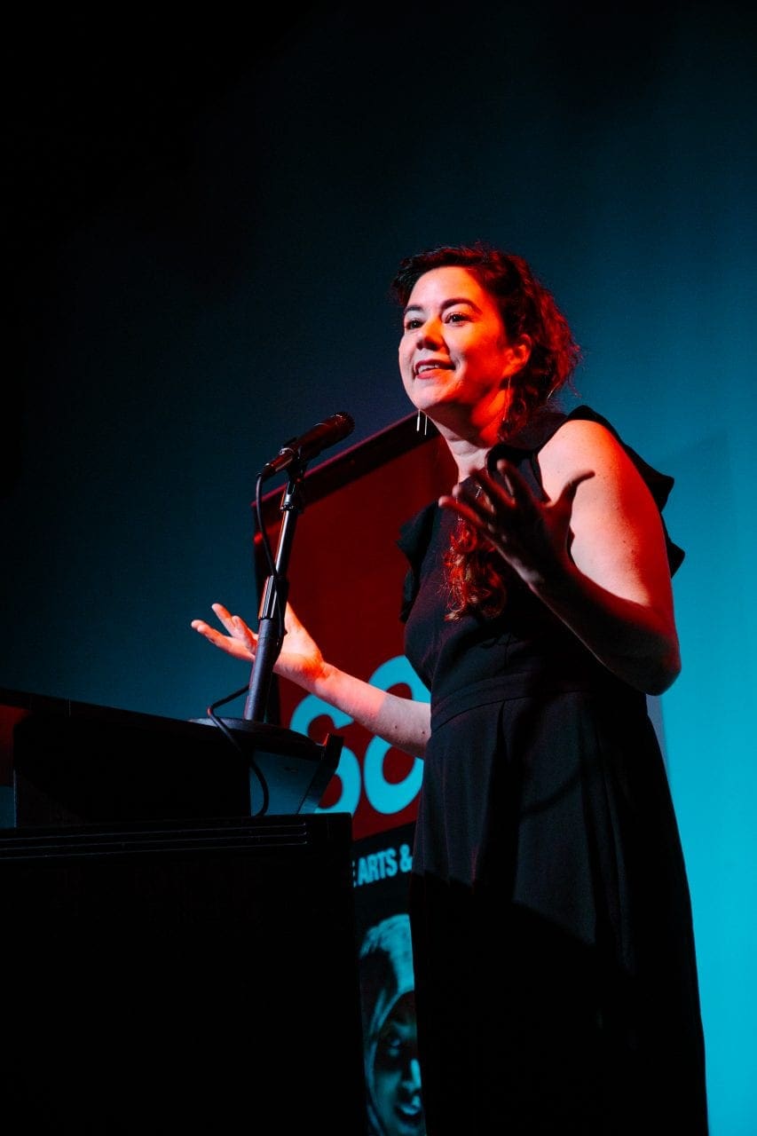 Rebecca Hoogs stands at a lectern looking out at the audience
