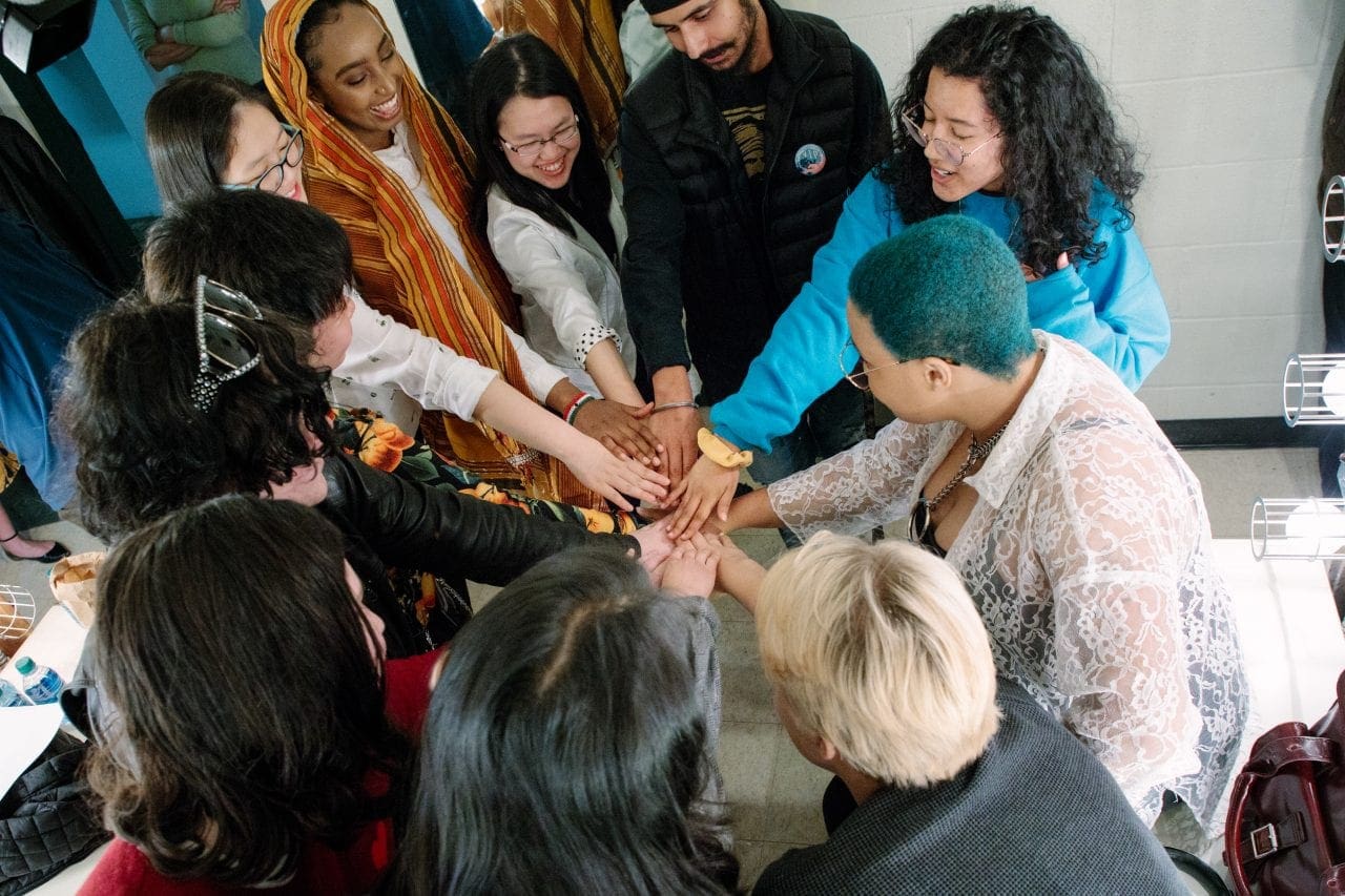 Youth Poet Laureate Finalists stand in a circle with one hand extended in the center