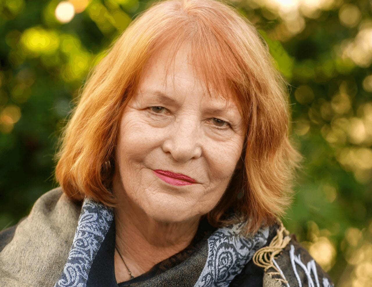 Close-up of Judith Roth, standing amid a blurred background of green, diffused light through trees.