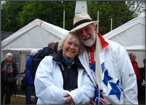 Sally smiles, wears a white coat and Robert smiles with his arms around Sally, wearing a white hat and coat