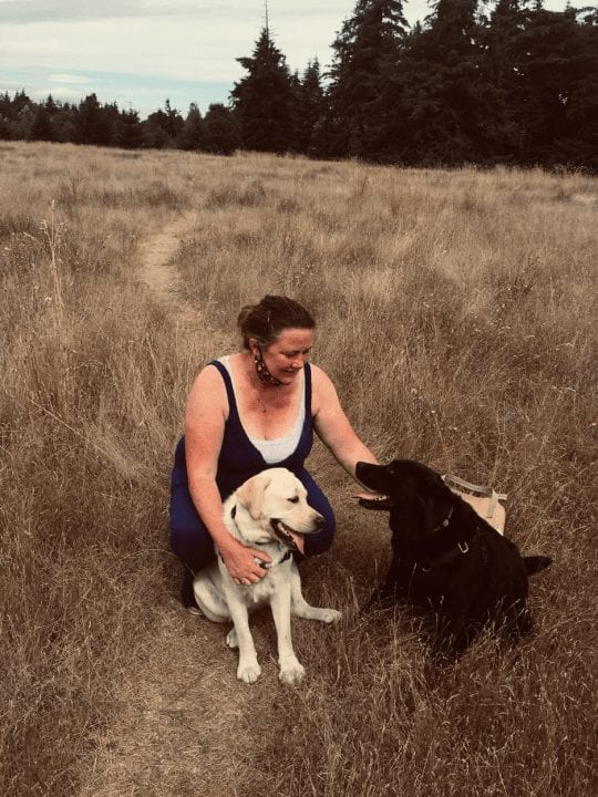 Liz Keenan is in a grassy field with a golden Labrador and a black Labrador