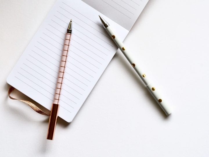 White lined notebook open with 2 pens beside it