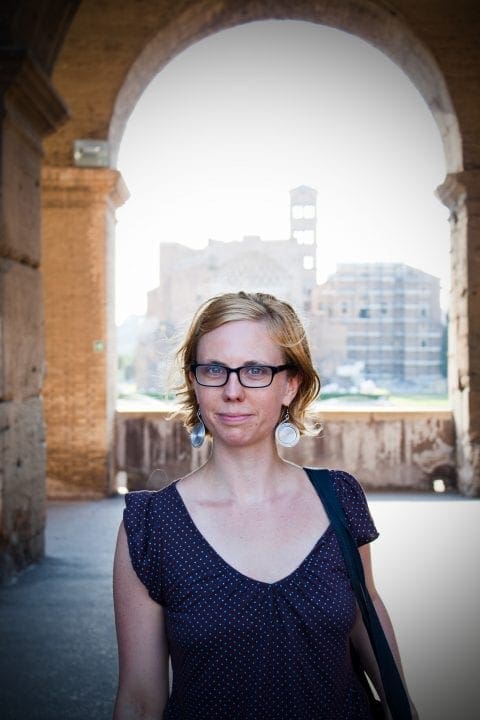 Sierra Nelson stands against a backdrop of a Roman archway, the Colosseum behind her.